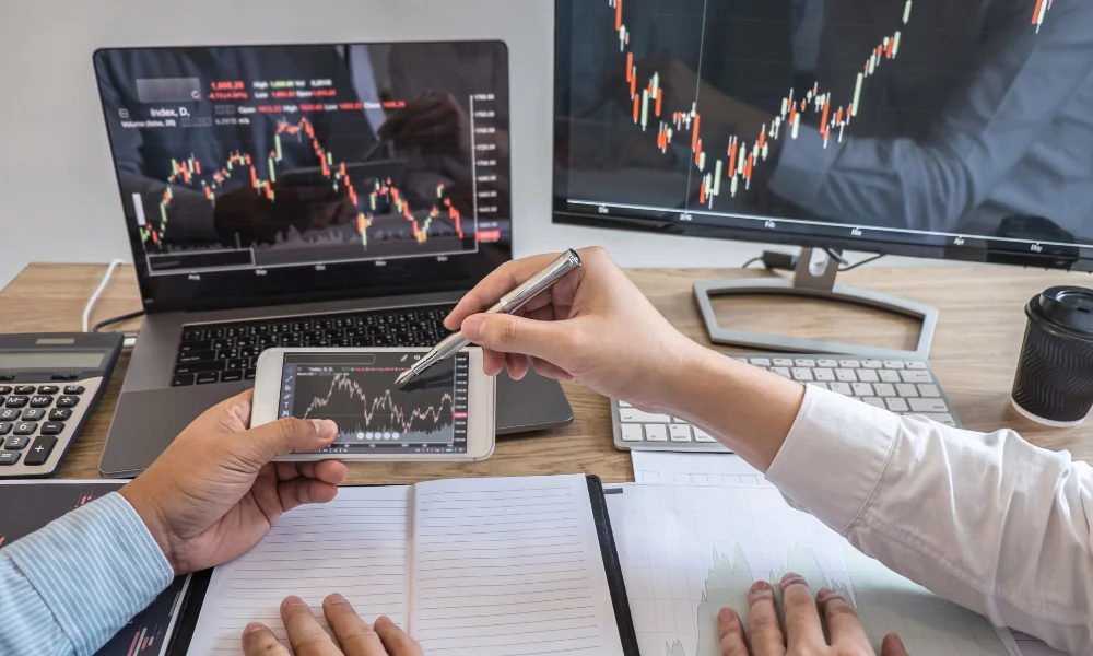 Profesionales analizando gráficos de trading en laptop, monitor y celular